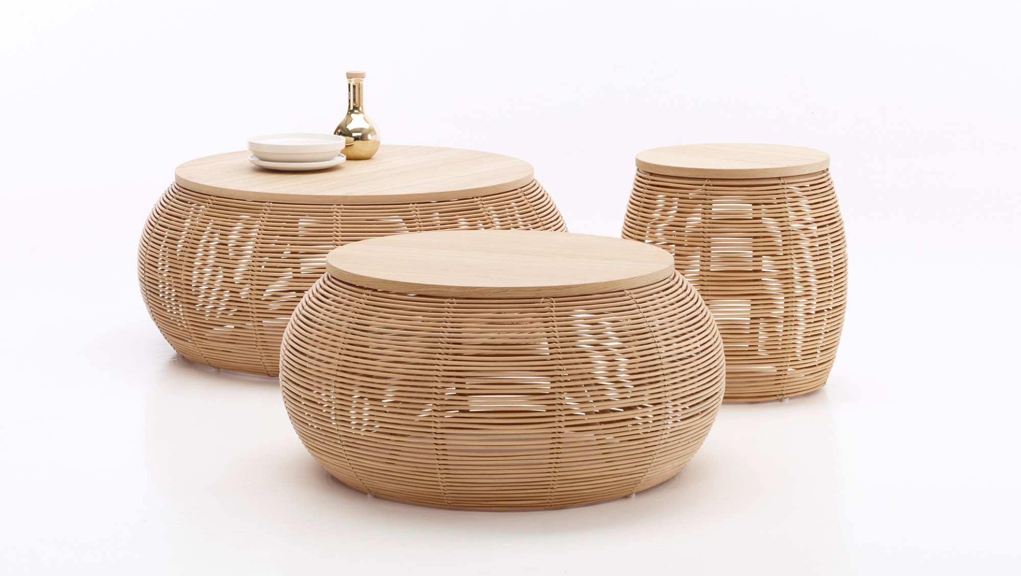 Set of Vincent Sheppard Vivi side tables in natural rattan with round wooden tops, displayed with a golden vase and stacked white plates