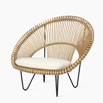 Vincent Sheppard Roy Cocoon-Sessel aus natürlichem Rattan mit gebogenem, offen gewebtem Design und einem weichen weißen Kissen auf schlanken schwarzen Metallbeinen.