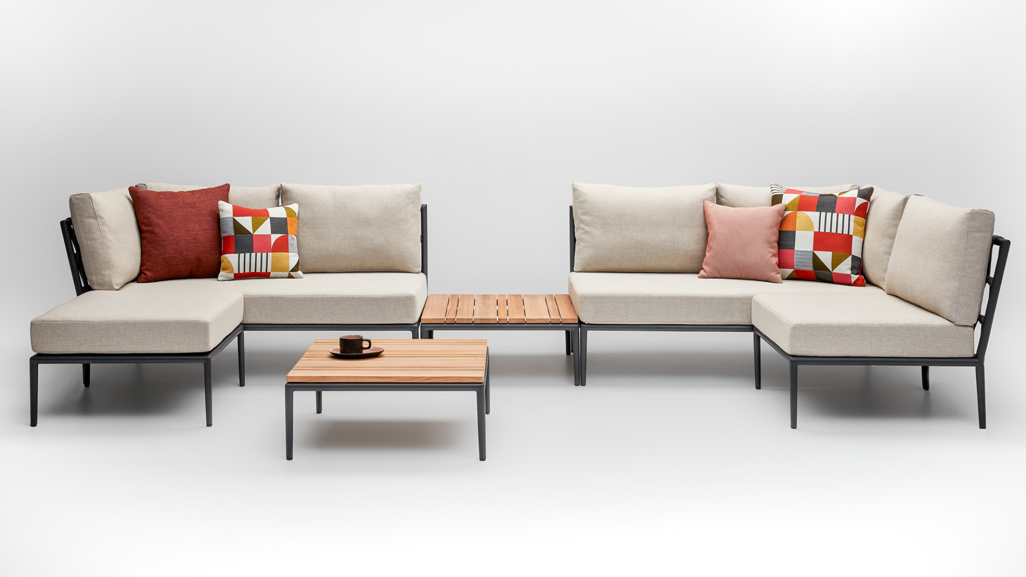 Vincent Sheppard Leo modulaire sofa met amandelkleurige kussens, kleurrijke geometrische en spicy rode kussens, en een onbewerkt teakhouten salontafel met een lavakleurig frame.