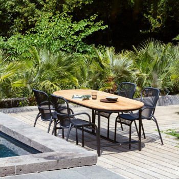 Poolside dining area featuring a Vincent Sheppard Wicked dining table with a natural wood top and matching Loop dining chairs, surrounded by lush greenery.