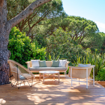 Buitenlounge bij Jas de Tournel met Vincent Sheppard's wicker loungeset, inclusief een bank, fauteuils en een ronde salontafel, omgeven door weelderig groen en hoge bomen.