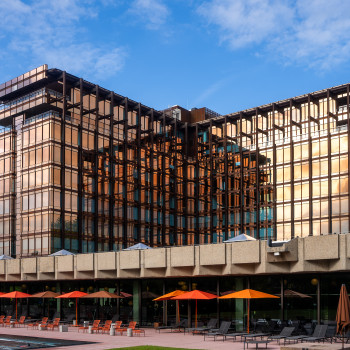 Mix Brussels Hotel with its iconic Royal Belge building, featuring a terrace with orange and red parasols, poolside lounge chairs, and a footrest by Vincent Sheppard on a sunny day.