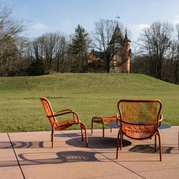 Mix Brussel hotelterras met terracotta kleurige Loop loungestoelen en voetensteunen van Vincent Sheppard, met uitzicht op een tuin en een historisch gebouw in de verte.