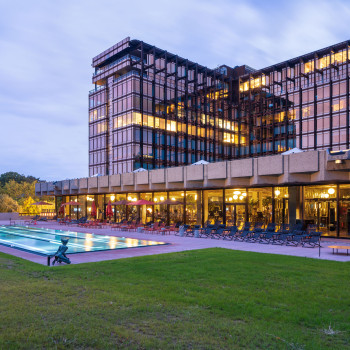 Evening view of the Mix Brussels Hotel with the iconic Royal Belge building, featuring a lit-up terrace and swimming pool area with lounge chairs.