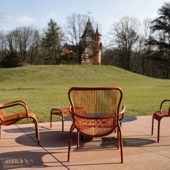 Terracotta kleurige Loop loungestoelen en voetensteunen van Vincent Sheppard op een terras bij het Mix Brussel hotel, met uitzicht op een tuin en een historisch gebouw op de achtergrond.