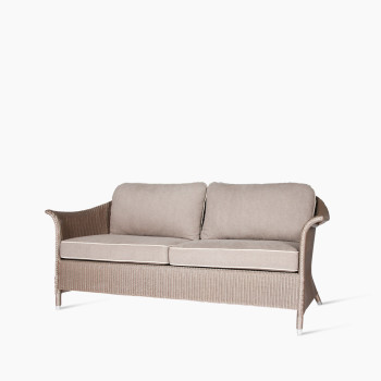 Angled view of the Vincent Sheppard Victor 2.5-seater lounge sofa with a woven frame in natural tones and taupe cushions