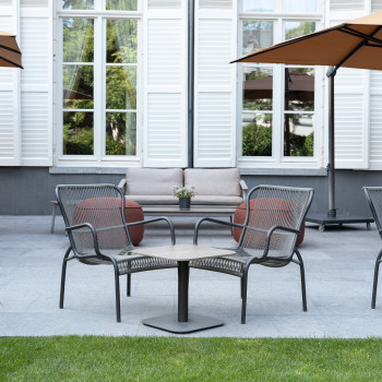 Outdoor seating area at Duke's Palace in Brugge with Loop lounge chairs, round orange poufs, and a beige outdoor sofa under large umbrellas.