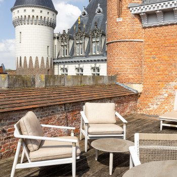 Terrasse sur le toit au Duke's Palace à Brugge avec des fauteuils lounge David et des tables rondes, avec vue sur les tours et l'architecture ornée du château.