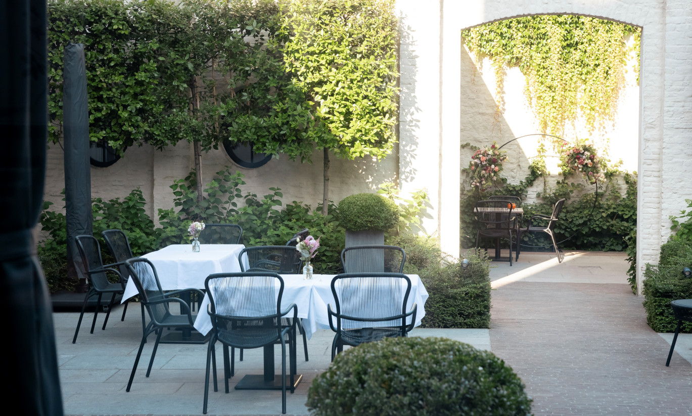 Outdoor dining area at Cobergher Hotel in Kortrijk with tables covered in white tablecloths, Loop dining chairs, and surrounding greenery.