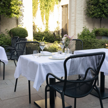 Espace de restauration en plein air à l'hôtel Cobergher à Courtrai avec nappes blanches, chaises de salle à manger Loop et arrangements floraux.