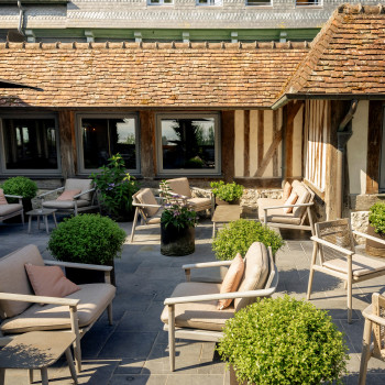 Terrasse à La Ferme Saint-Siméon avec des chaises lounge David, des chaises de salle à manger, des tables de salle à manger, des canapés lounge et des tables d'appoint, décorée avec des plantes en pot.