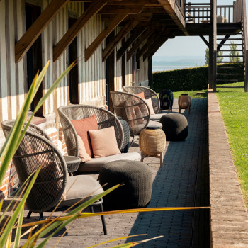 Gemütliche Ecke bei La Ferme Saint-Siméon mit Kodo Cocoon Stühlen, Kissen, Tika Laternen mit Stahl- und Teakholzsockel, die einen komfortablen Außenbereich schaffen.