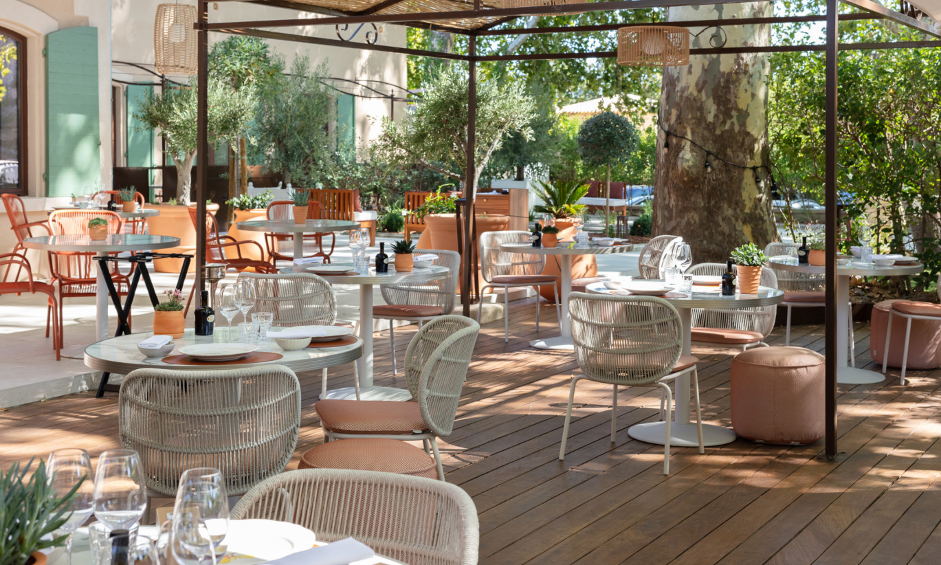 Espace de restauration en plein air à La Bastide Bourelly avec des chaises Kodo en Dune White et des chaises Loop en Terracotta, entouré de verdure luxuriante et d'un sol en bois.