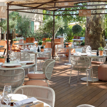 Espace de restauration en plein air à La Bastide Bourelly avec des chaises Kodo en Dune White et des chaises Loop en Terracotta, entouré de verdure luxuriante et d'un sol en bois.