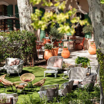 Gartensitzbereich bei La Bastide Bourrelly mit Roy Lazy Chairs, Kodo Cocoon-Stühlen und Loop-Essstühlen in Terrakotta, umgeben von Grün und Topfpflanzen.