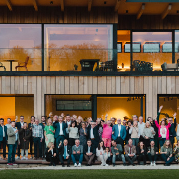 Gruppenfoto des Vincent Sheppard-Teams vor ihrem Showroom, einem modernen Holzgebäude mit großen Glasfenstern.