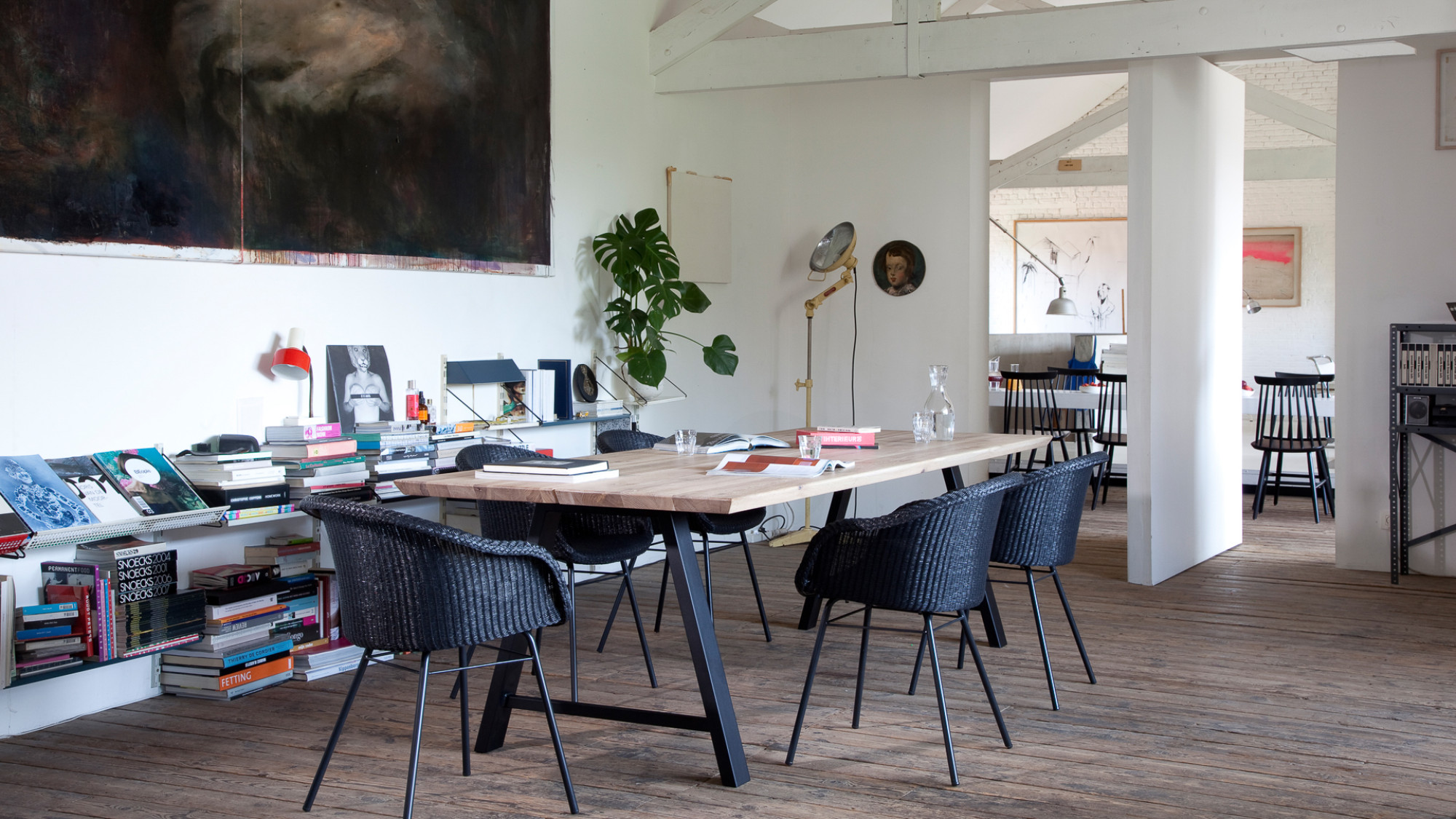 Eethoek met Vincent Sheppard Avril eetkamerstoelen met een stalen A-onderstel en een Albert tafel in een moderne, kunstzinnige ruimte met houten vloeren en planken vol boeken.