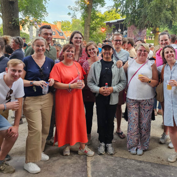 Groepsfoto van het Vincent Sheppard-team op een buitenfestival met lachende teamleden die drankjes vasthouden, omringd door bomen en andere festivalgangers.