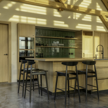 Kitchen with Teo bar stools by Vincent Sheppard, featuring black plywood seats and backs, set around a wooden island with green tiled backsplash.