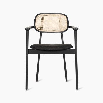 Front view of the Titus dining armchair by Vincent Sheppard featuring a black upholstered seat and woven rattan backrest.