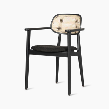 Titus dining armchair by Vincent Sheppard, featuring a black upholstered seat and woven rattan backrest, shown from a 45-degree angle.