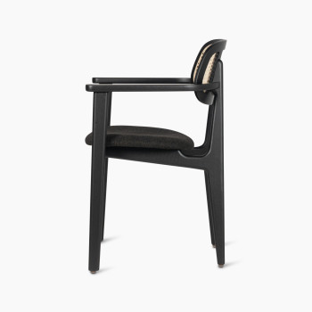 Side view of the Titus dining armchair by Vincent Sheppard, featuring a black upholstered seat and a woven rattan backrest.