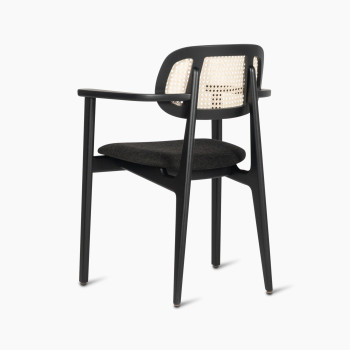  Titus dining armchair by Vincent Sheppard, featuring a black upholstered seat and a woven rattan backrest, shown from a 135-degree angle.