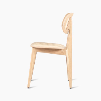 Side view of a Titus dining chair in natural varnished oak with a woven cane backrest and seat.