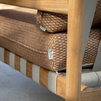 Close-up of the Vincent Sheppard Oda collection chair, featuring Sienna-colored cushions with a woven texture and wooden armrests.