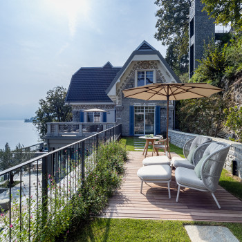 Terras bij Breakwater Bellagio met Kodo Cocoon stoelen en voetenbanken, met een grote parasol en uitzicht op het Comomeer en de bergen.