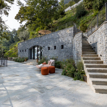 Buitenterras bij Breakwater Bellagio met een Kodo-daybed en oranje poefs, tegen een stenen muur met een trap die naar een tuin leidt. Een standbeeld staat aan de voet van de trap.