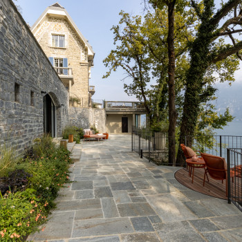 Terrasse en pierre à Breakwater Bellagio avec la collection Loop en couleur Terracotta, comprenant deux chaises longues sur une plate-forme en bois circulaire surplombant le lac de Côme, avec des sièges supplémentaires plus loin sur la terrasse.