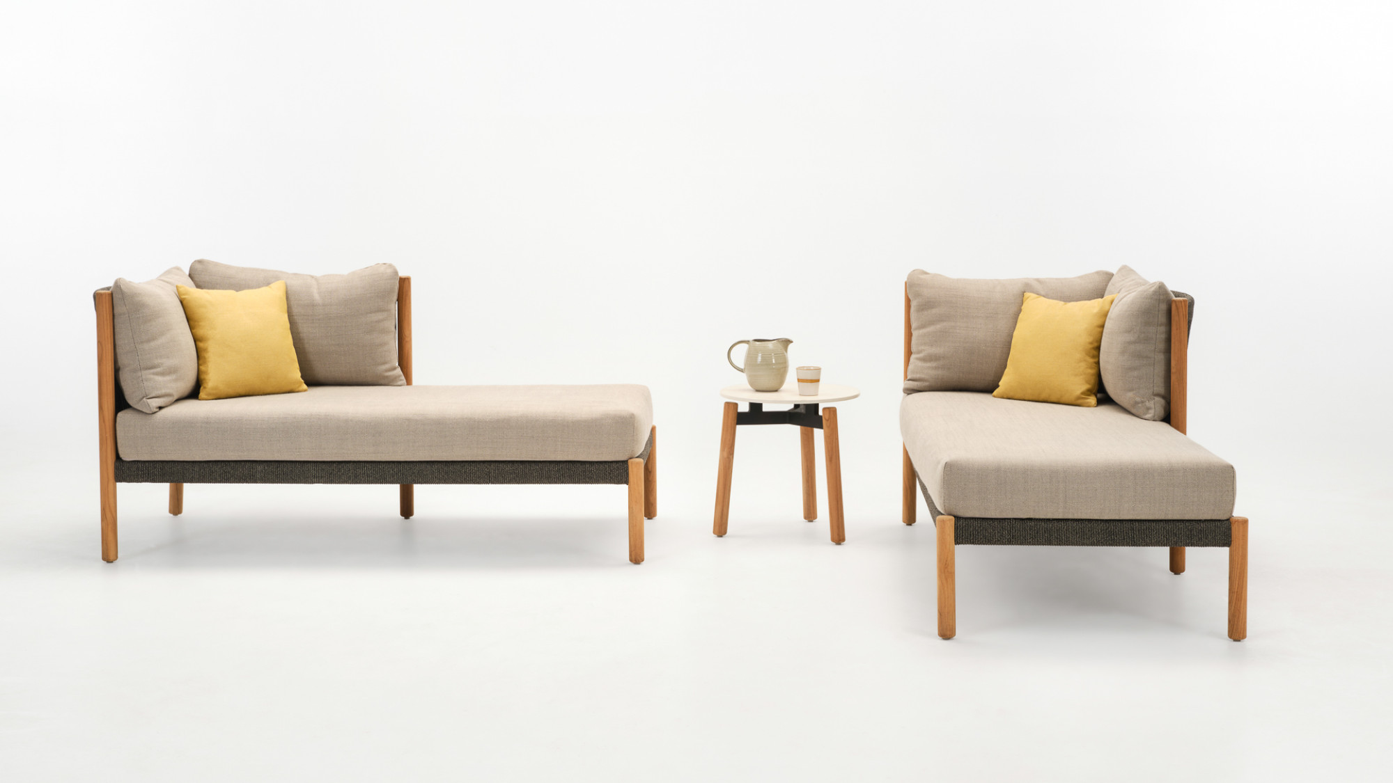  Two Vincent Sheppard Lento chaise longues in teak with stone dust cushions, accompanied by a Lento side table in untreated teak and Portland finish, decorated with a ceramic jug and cup.