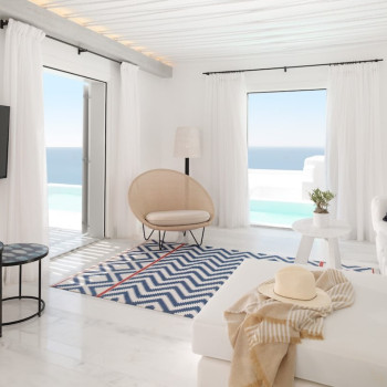 Salon au Mykonos Riviera Hotel & Spa avec fauteuil Joe Cocoon de Vincent Sheppard, canapé blanc, tapis à motifs et vue sur la mer.