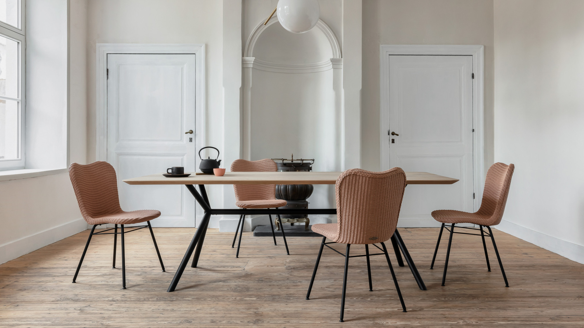 Salle à manger avec chaises Vincent Sheppard Lily au piètement en acier A autour d'une table en bois moderne, dans une pièce minimaliste avec murs blancs et parquet en bois.