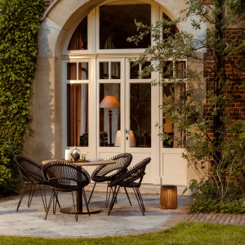 Outdoor patio at a country house with Roxy dining chairs, a Ronda bistro table, and Maya lamps. The setting features ivy-covered walls and a view of a garden.