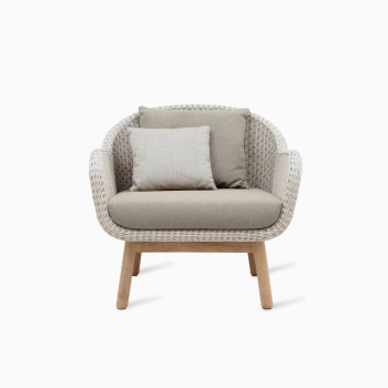 Anton lounge chair by Vincent Sheppard with a wicker seat in Old Lace colour and a teak wood frame, featuring soft beige cushions.