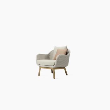 Side view of the Anton lounge chair by Vincent Sheppard with a wicker seat in Old Lace colour, a teak wood frame, and beige cushions, featuring a pink accent pillow.