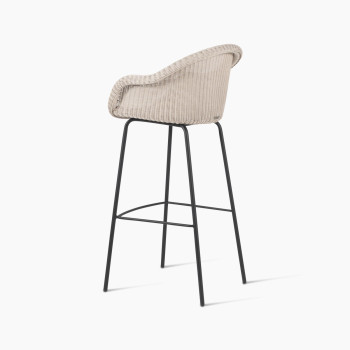 Edgard barstool by Vincent Sheppard, viewed from the back at a 135-degree angle, featuring an old lace-coloured wicker seat and a black steel base.