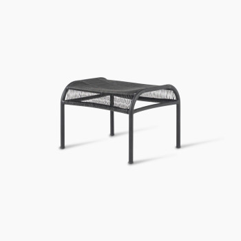  Angled view of the Loop footrest in black by Vincent Sheppard, featuring a curved metal frame with a woven Lloyd Loom surface, designed for resting feet.