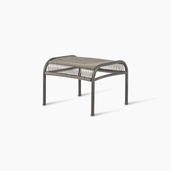 45-degree angled view of the Loop footrest in dark grey by Vincent Sheppard, showcasing a curved metal frame with a woven Lloyd Loom surface, designed for foot comfort and support.