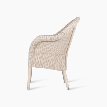 Mia dining chair in old lace colour, shown from the side view. The chair features a wicker frame with a curved backrest and armrests, offering a soft and elegant profile.