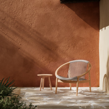 Espace extérieur avec le Frida Lounge Chair de Vincent Sheppard en dune white et la table d’appoint Anton en teck, placé contre un mur en terre cuite chaleureux. La lumière du soleil crée de douces ombres sur la surface texturée.