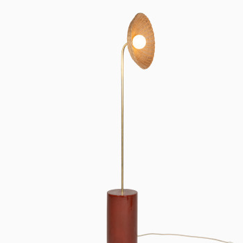 Arvin floor lamp with a curved brass stem, maroon ceramic base, and a rattan shade, emitting a warm glow.