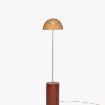 Packshot of the Arvin floor lamp featuring a cylindrical ceramic base in maroon, a slender brass stem, and a woven rattan dome-shaped shade.